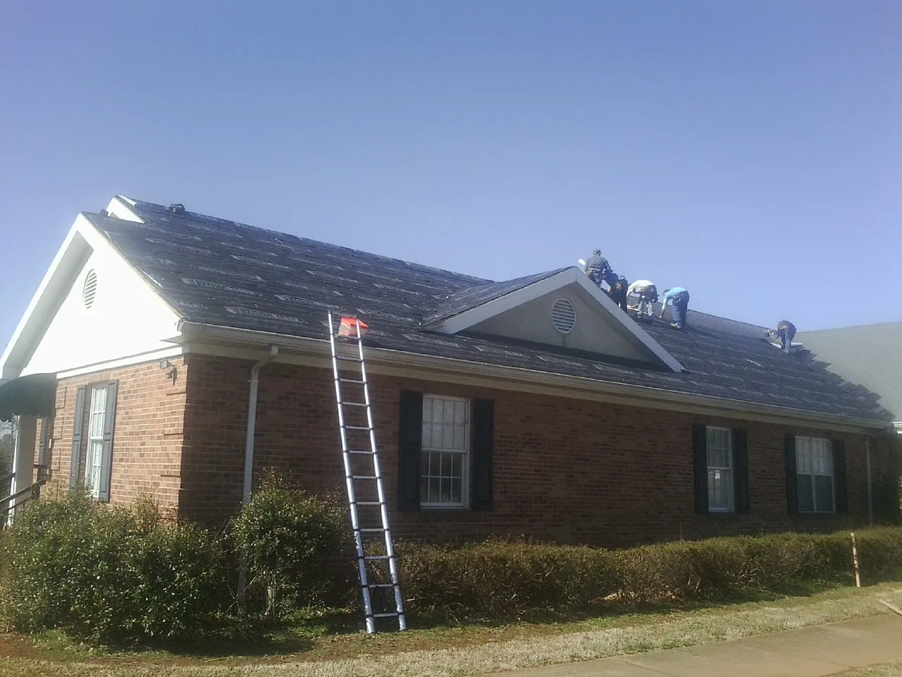 Crew tearing shingles off a brick ranch roof with a ladder set — Emergency Roof Repair work by our crew in Wapakoneta
