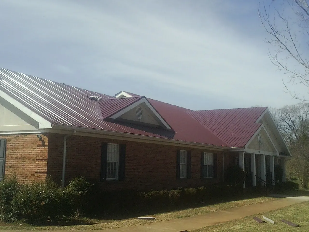 Red metal roof with gabled entries on a long brick building, from a Hail Damage Roof Repair job in Wapakoneta