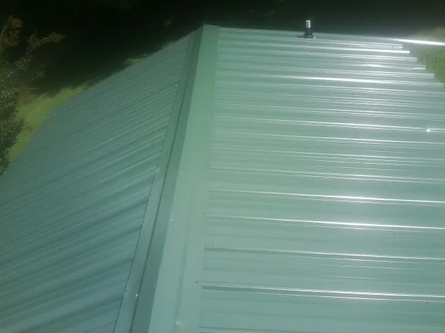 New green metal panels meeting at the ridge of a roof — Flat Roof Repair work by our crew in Wapakoneta