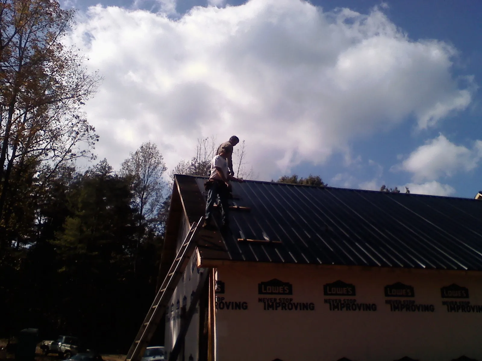 Roofer fastening dark metal panels high against a cloudy sky, from a Roof Inspection job in Wapakoneta