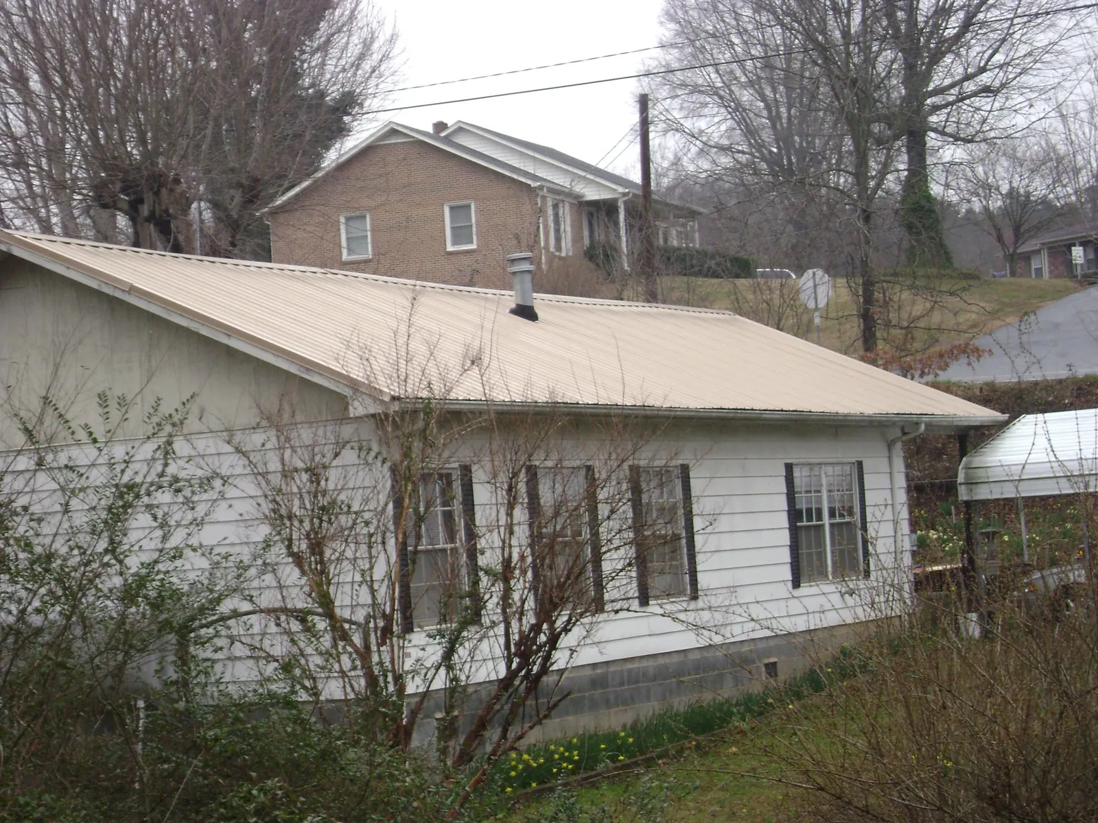 Tan metal roof on a white sided house set into a hillside — Commercial Roofing by Roofing Brothers in Wapakoneta
